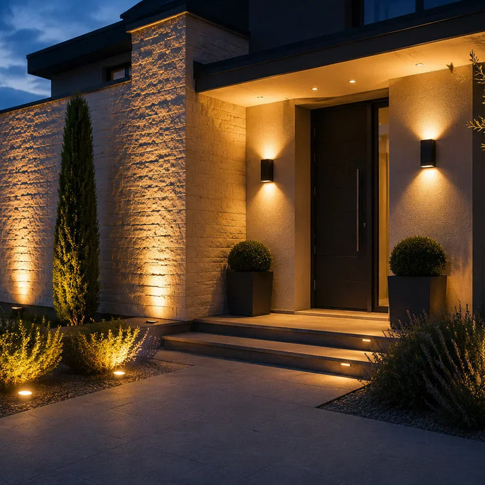 Facciata di casa illuminata di sera con faretti da terra orientati verso l'alto e applique da parete ai lati dell'ingresso